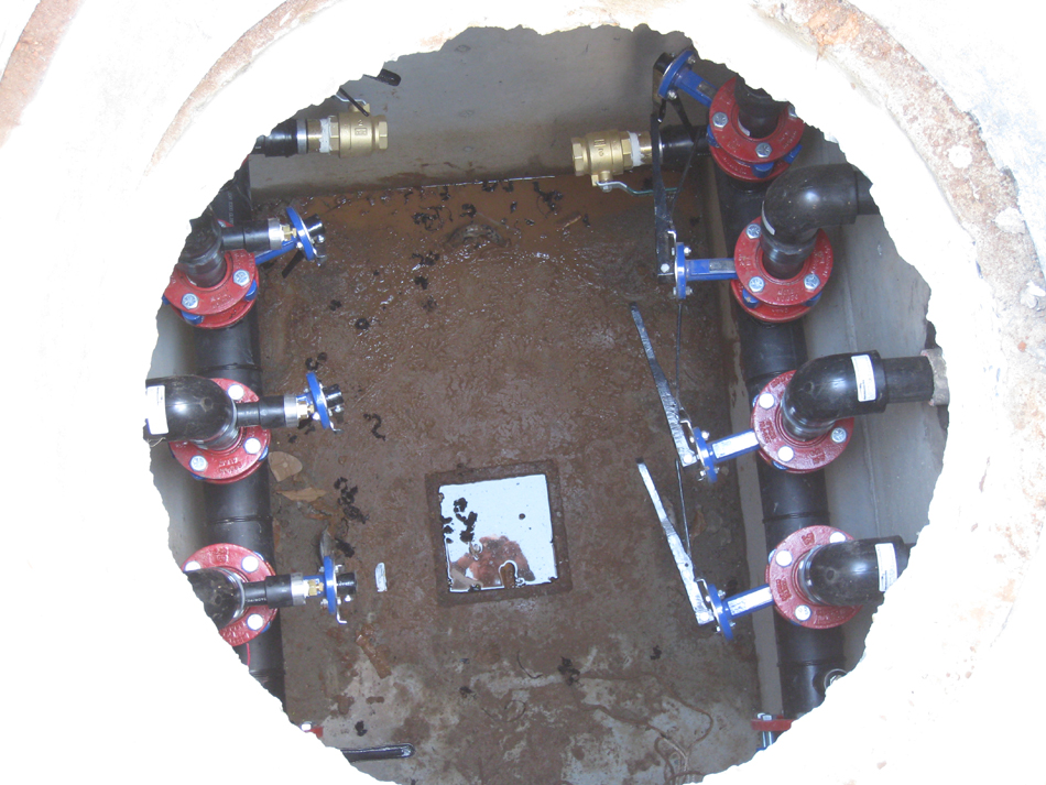 Geothermal/HVAC--Looking down manhole into vault at eight collection lines serving 32 wells (with water in the square)